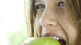 Junges Mädchen beißt in einen grünen Apfel