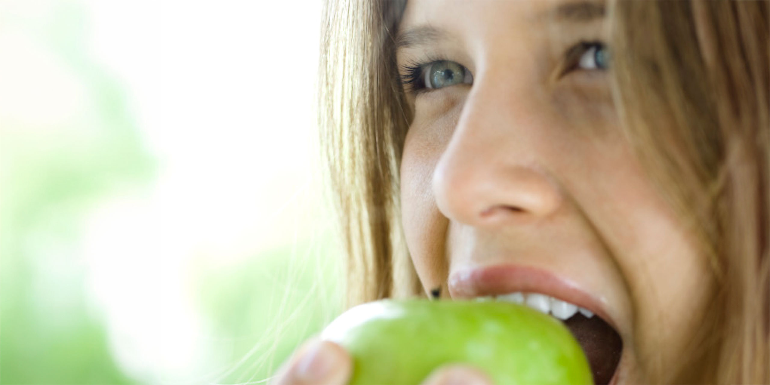 Junge Frau beißt herzhaft in einen grünen Apfel